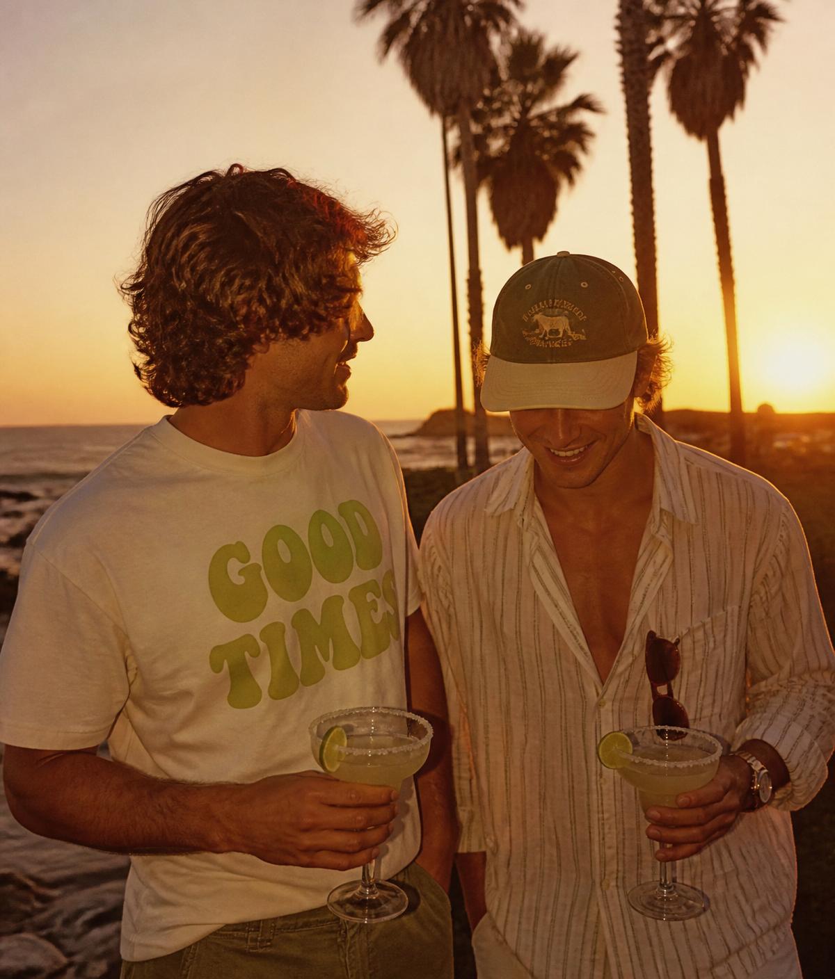 Two friends on Baja beach with margaritas at sunset